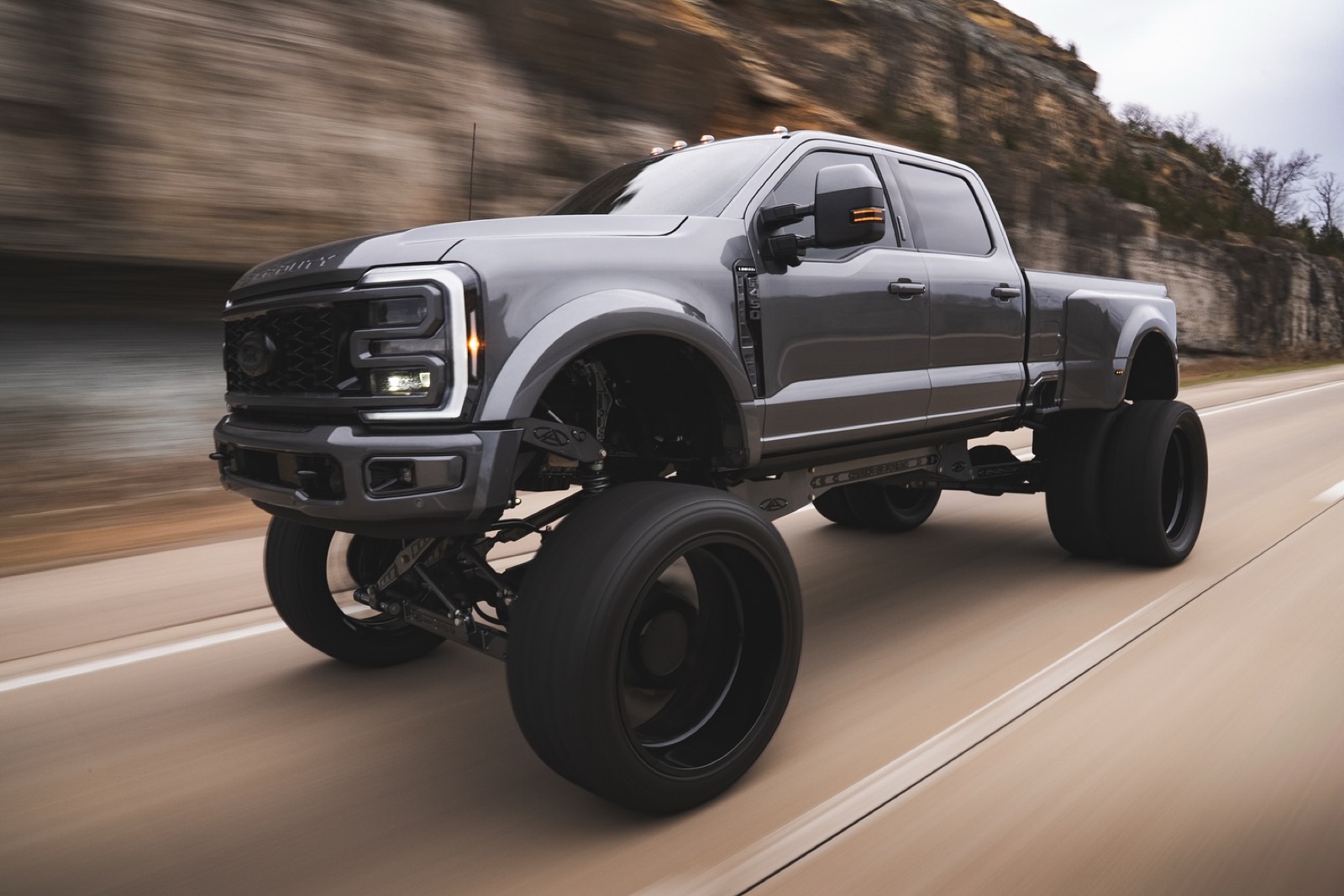 Same gray AnyLevel Ford F-450 driving on the road, photographed from the front passenger side