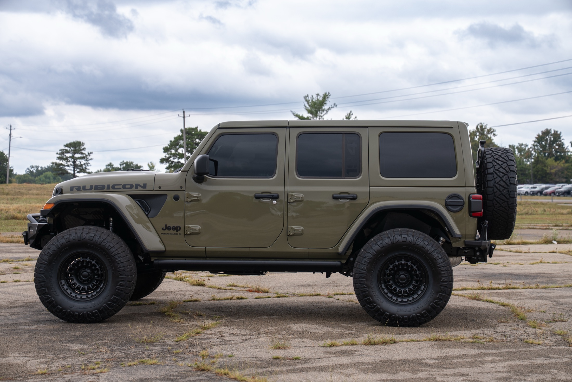 Side profile of an olive four-door Jeep Wrangler Rubicon with black wheels and off-road tires