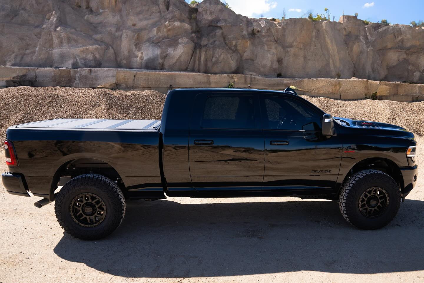 Side profile of the same black Ram 2500 Laramie Mega Cab showing its Carli stance, KMC wheels, Falken tires and bed cover