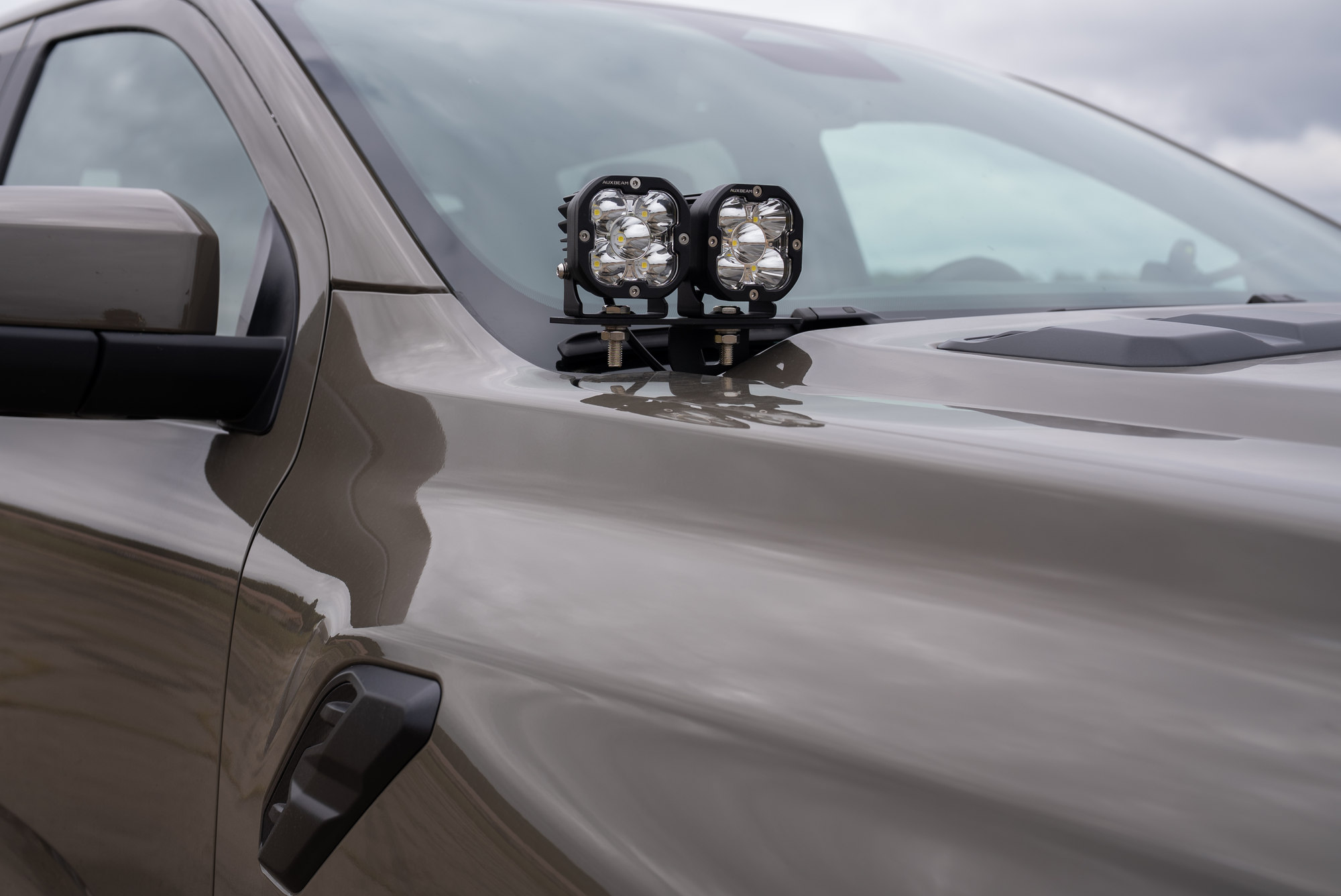 Two Auxbeam pod lights mounted on a bracket at the tan Ranger Raptor cowl beside the windshield