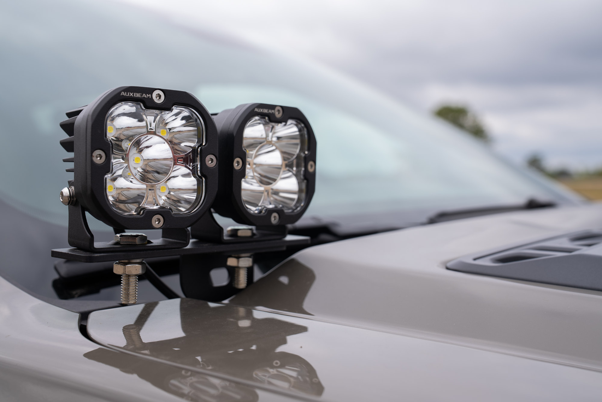 Close detail of the Auxbeam pod lights and cowl mounting bracket on the tan Ranger Raptor