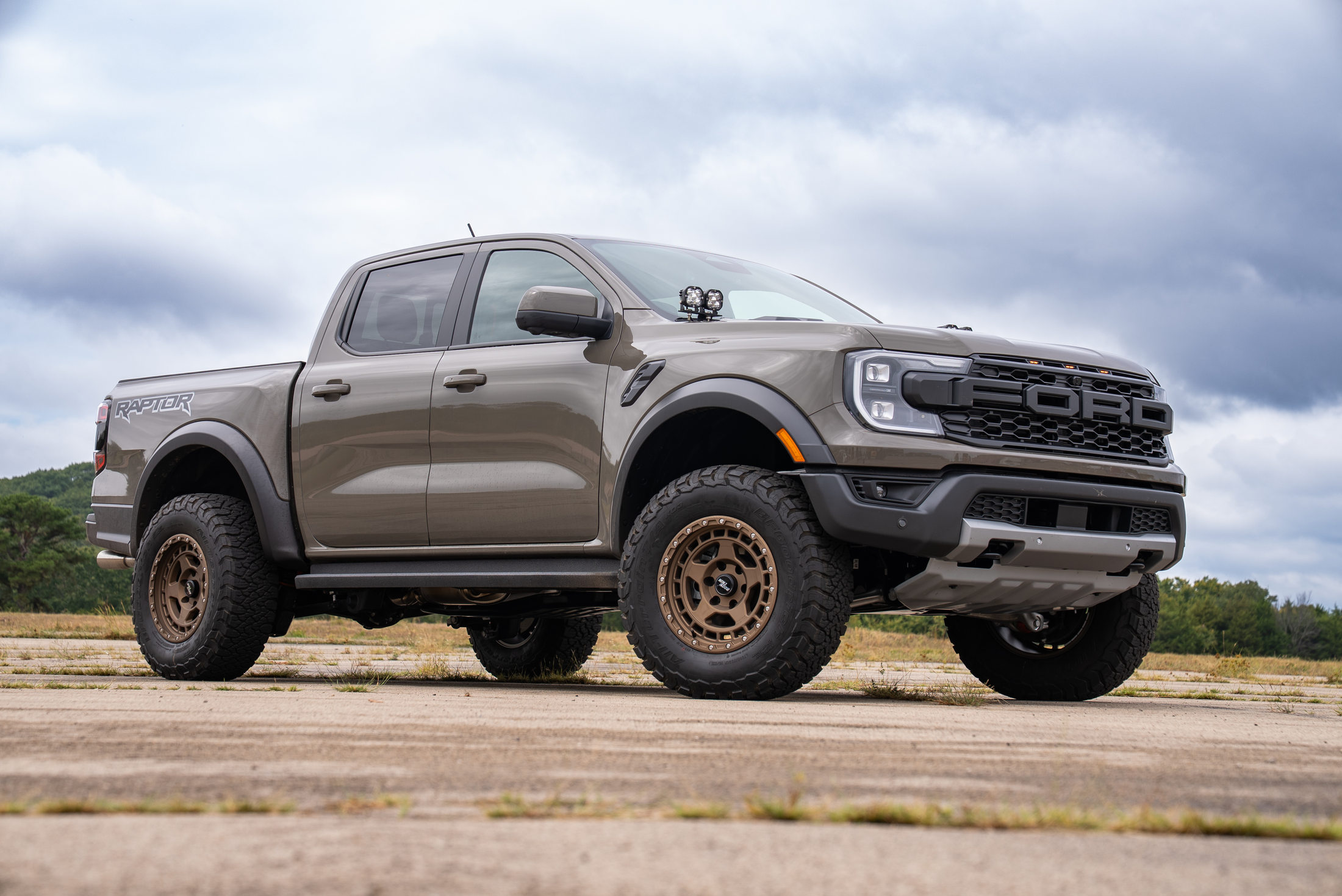 Tan Ford Ranger Raptor photographed from a low front-side angle with customer-supplied wheels and tires
