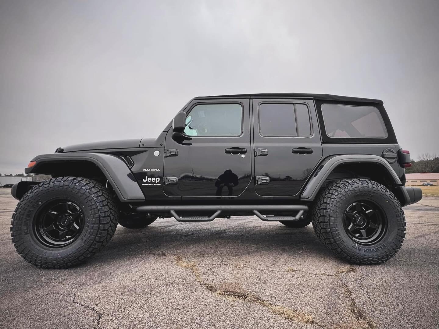 Side profile of the black 2024 Wrangler Sahara showing its Rough Country tubular steps and 35-inch tires